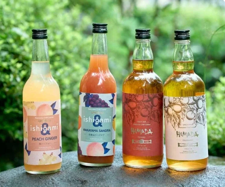 緑豊かな背景をバックに、4本の異なるリキュールまたは梅酒のボトルが並べられています。左の2本は「ishigami」ブランドのピーチジンジャーと和歌山サングリア、右の2本は「HAMADA」ブランドのジンジャーとバニラ風味とみられる製品です。