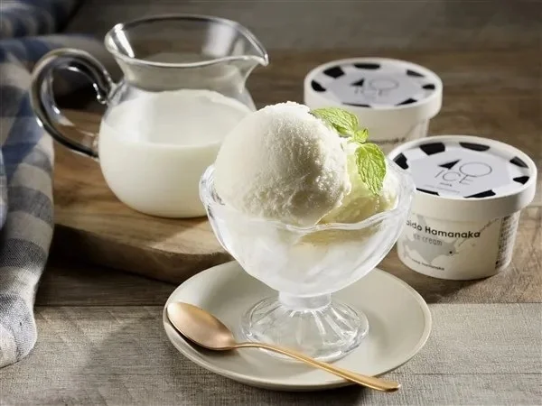 透明な器に盛られたバニラアイスクリームと、牛乳の入ったピッチャー、そしてカップ入りアイスクリームが木製のテーブルに置かれています。爽やかなミントが添えられた、涼しげなデザートの風景です。