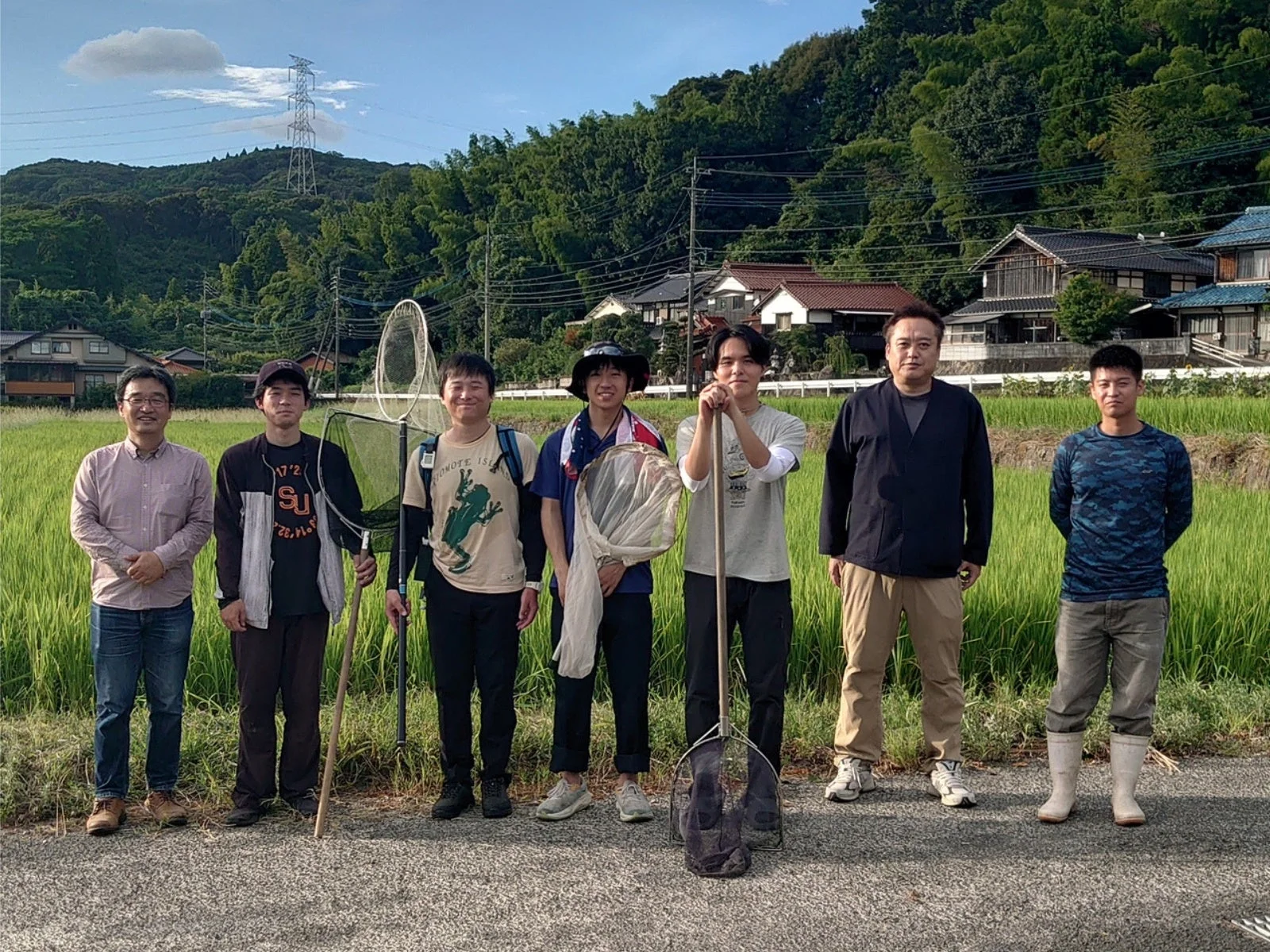 田んぼと山を背景に、網を持った人々を含むグループ