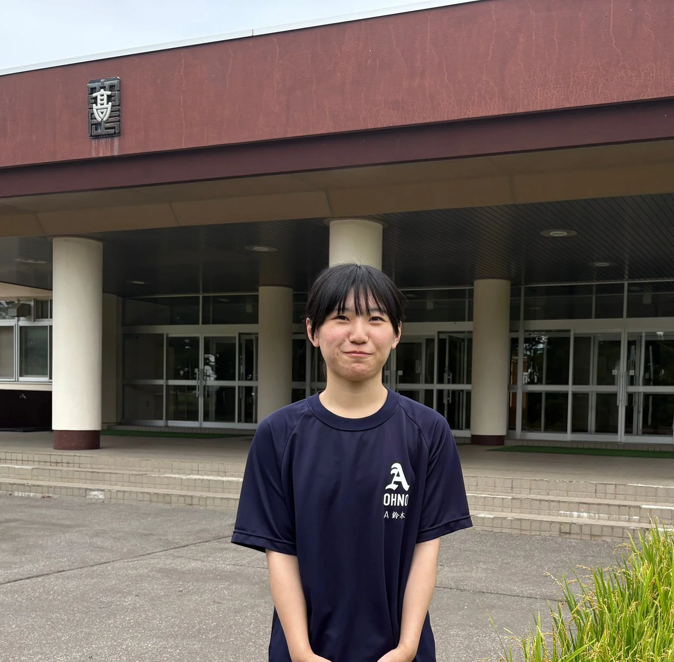学校らしき建物の前で立つ女性生徒