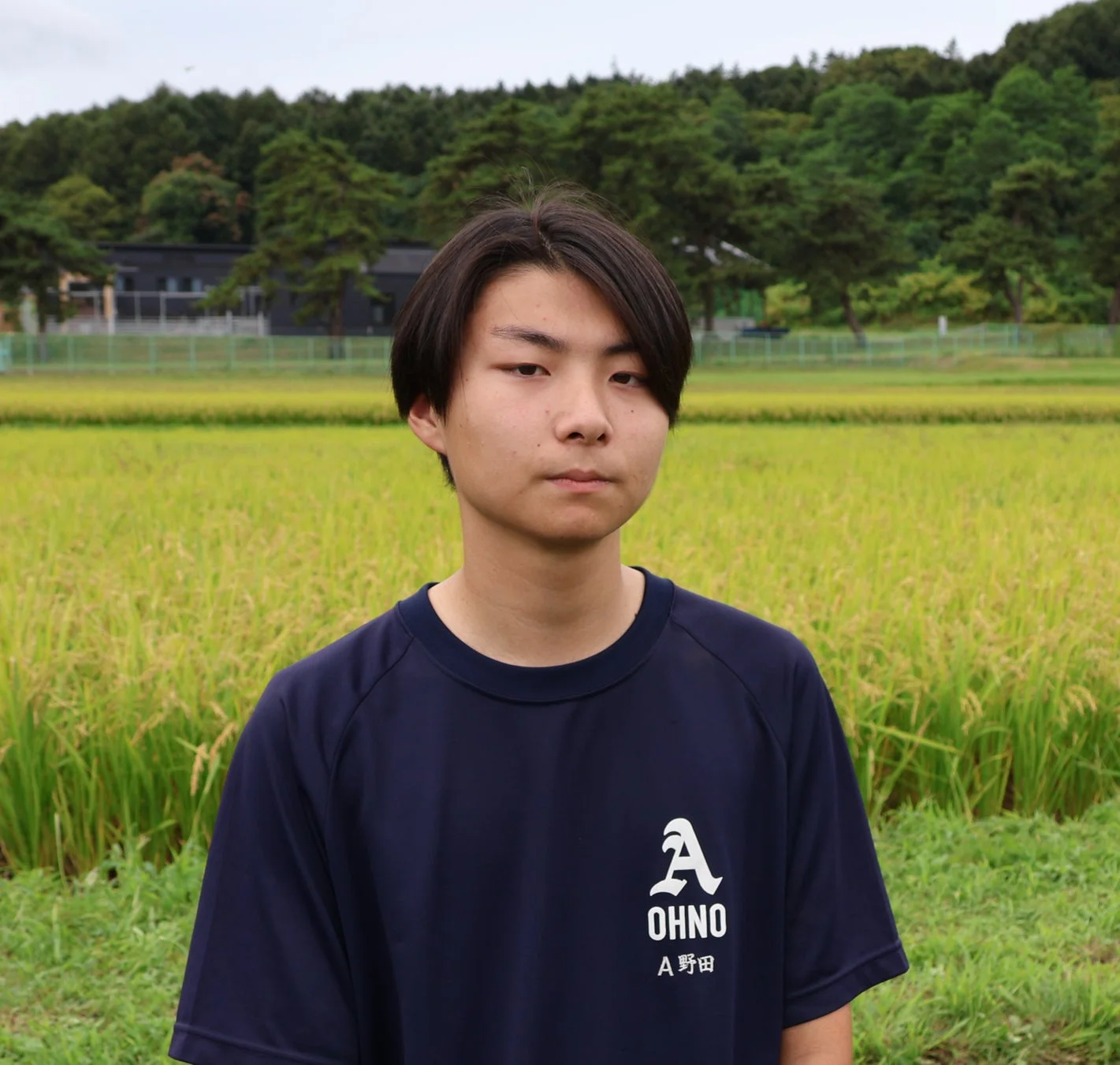 田んぼを背景に立つ男性生徒