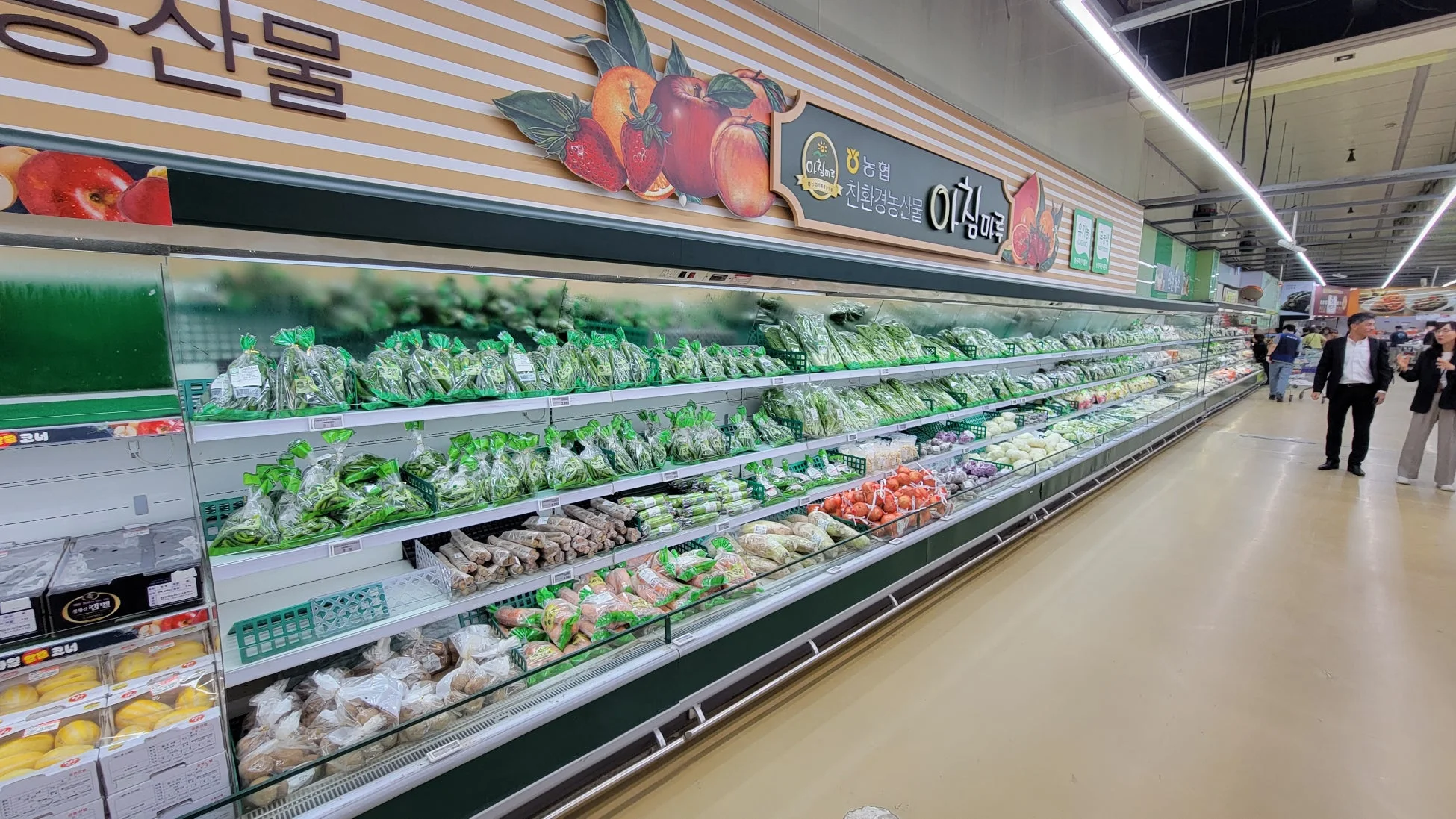 韓国のスーパーマーケットの生鮮食品売り場です。広々とした陳列棚には、袋詰めされた様々な野菜や果物がきれいに並べられています。