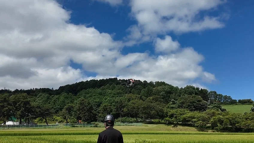 田んぼでドローンを見上げる人々