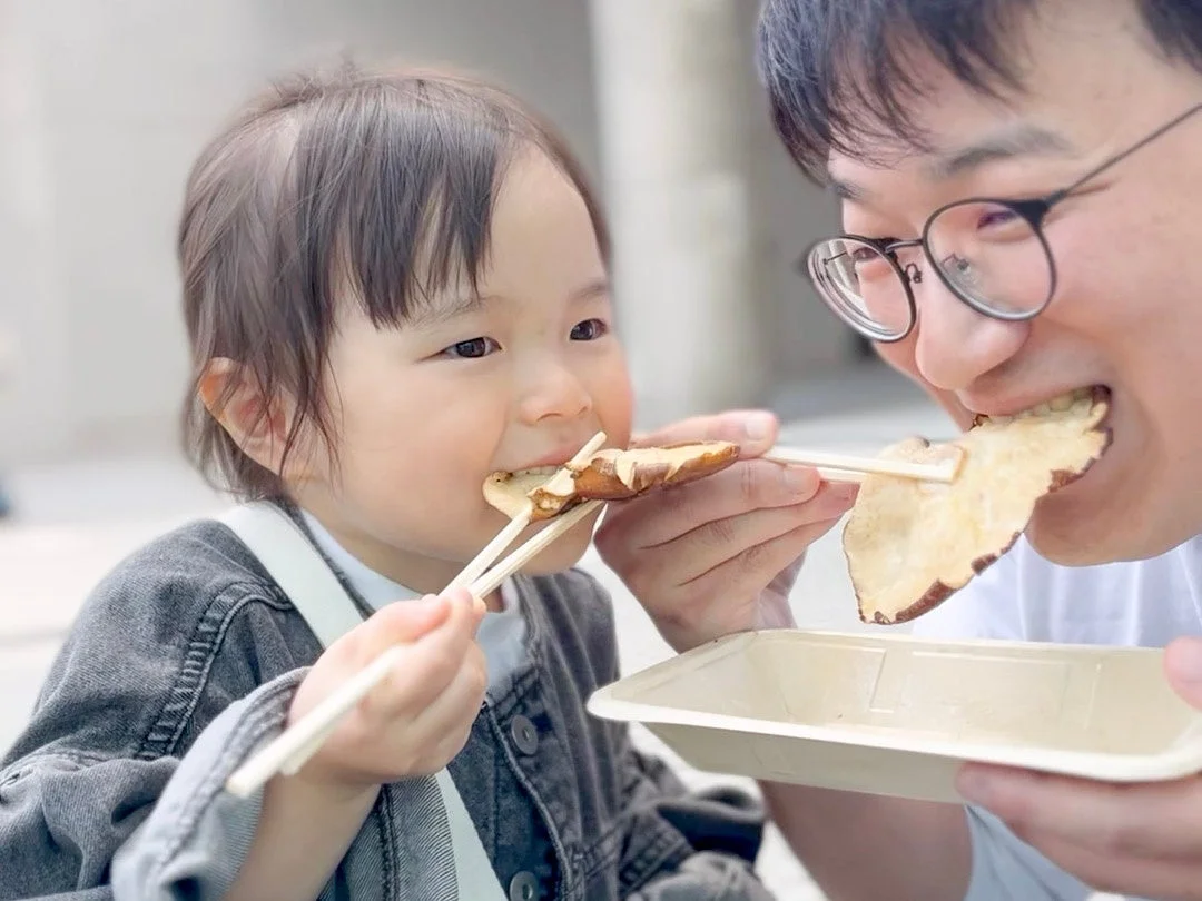 親子が串に刺さった食べ物を頬張る様子