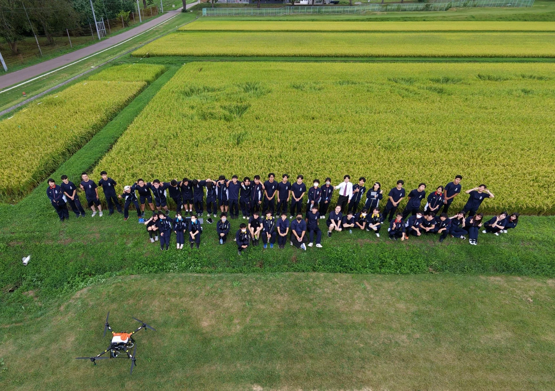 田んぼの前で集合写真を撮る学生と教員らしきグループ