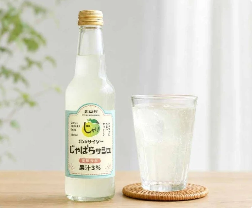 じゃばらサイダーの瓶とグラスが木製のテーブルに置かれています。グラスには氷と炭酸飲料が入っており、爽やかな印象を与えています。