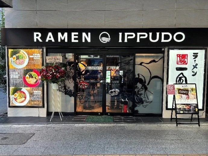 ラーメン一風堂の店舗外観。看板には店名とメニューが示され、赤丸クラシック、白丸モダン、からか麺が確認できる。入り口には花が飾られ、A型看板には「CLOSED」と表示されている。