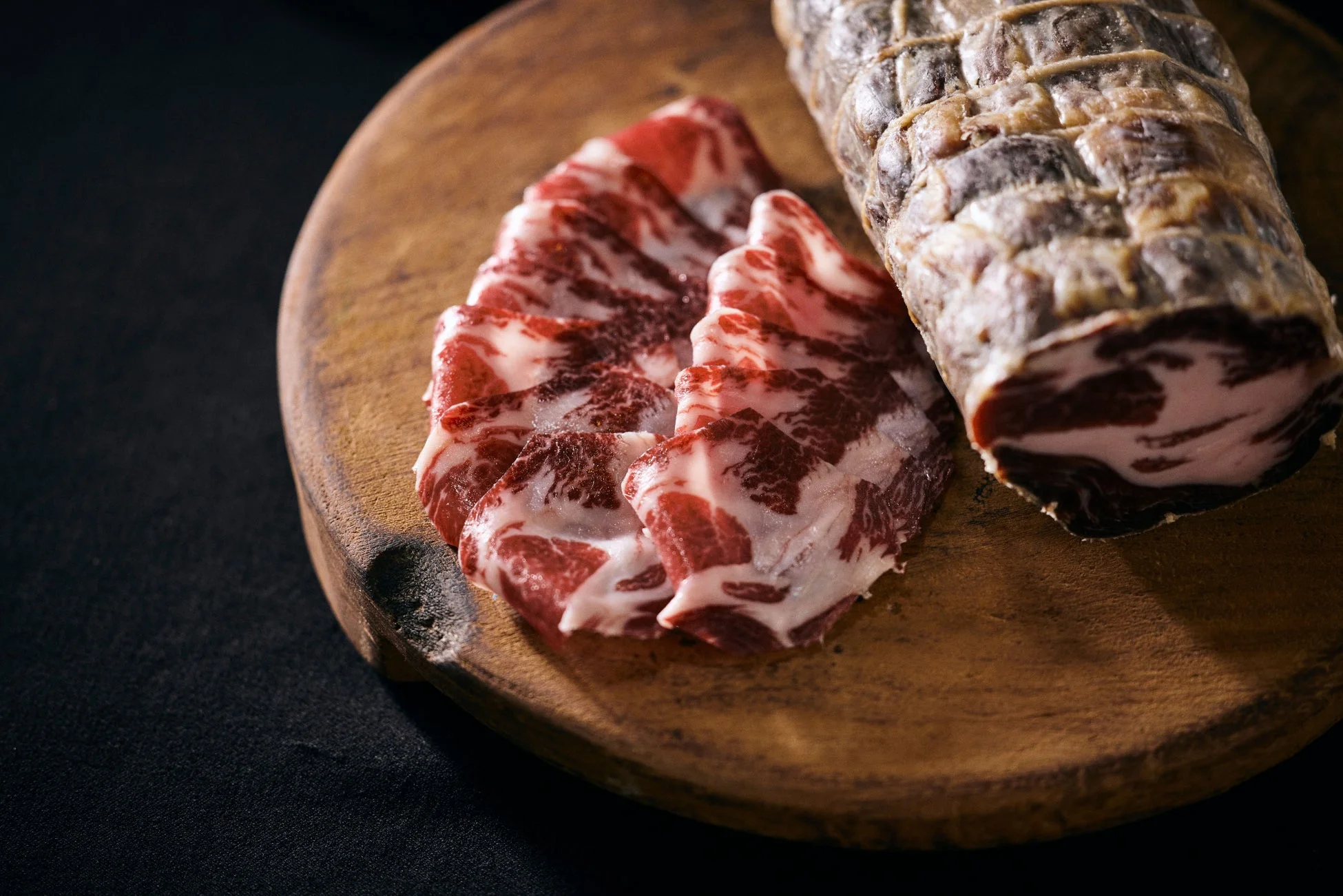 木製の板に盛り付けられた、薄切りの加工肉と塊の加工肉のクローズアップです。赤身と脂身の美しいコントラストが食欲をそそり、高級感のあるおつまみや前菜にぴったりな一品です。
