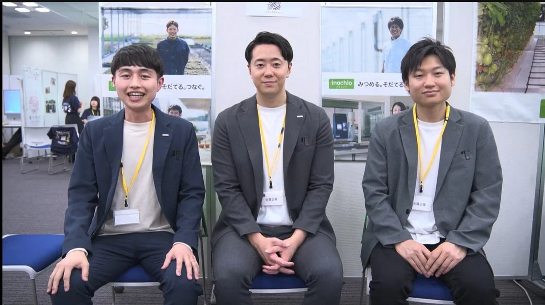 3人の若い男性が並んで座り、カメラに向かって笑顔を見せています