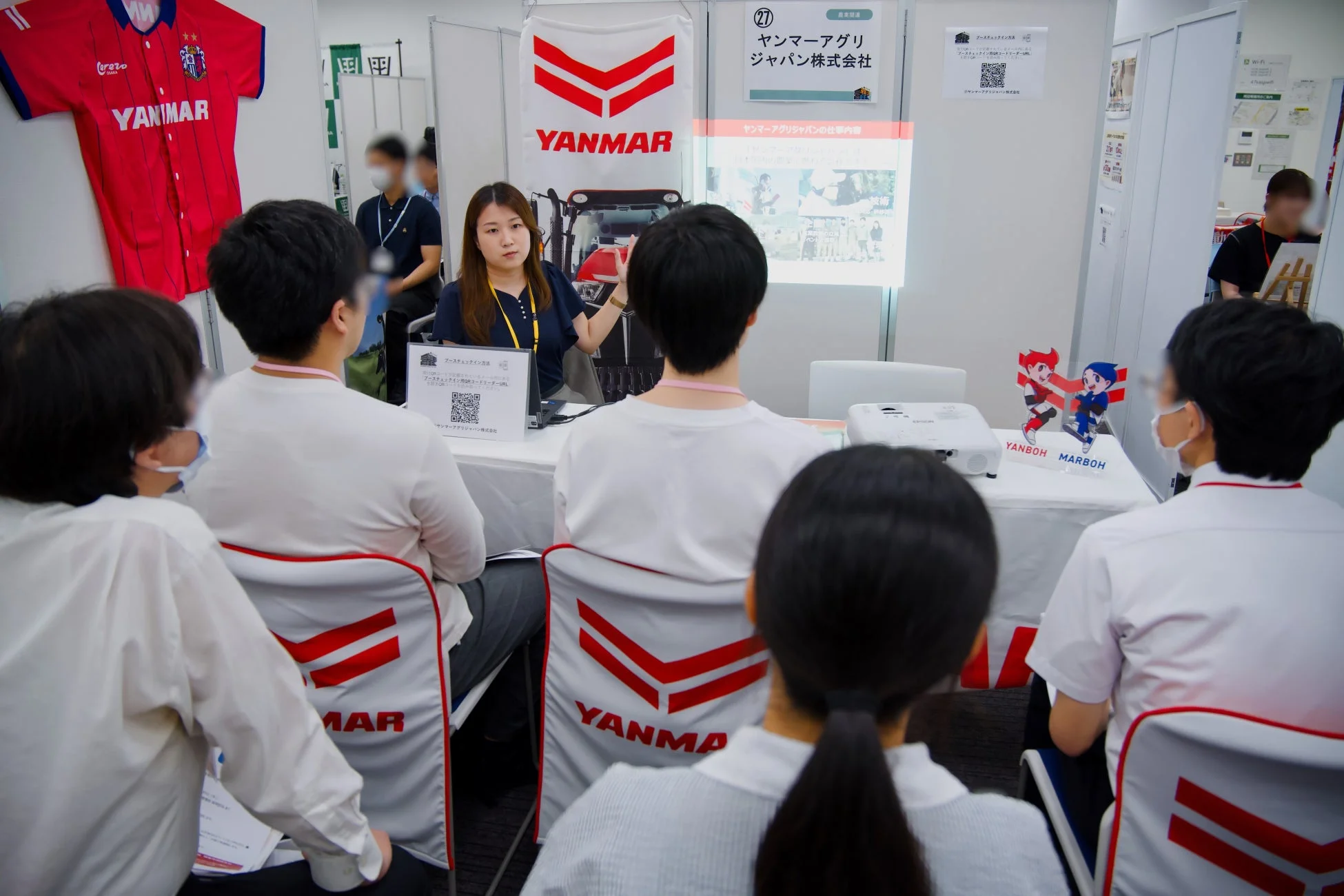 ヤンマーアグリジャパン株式会社のブースで、担当者が参加者たちに会社説明を行っている様子