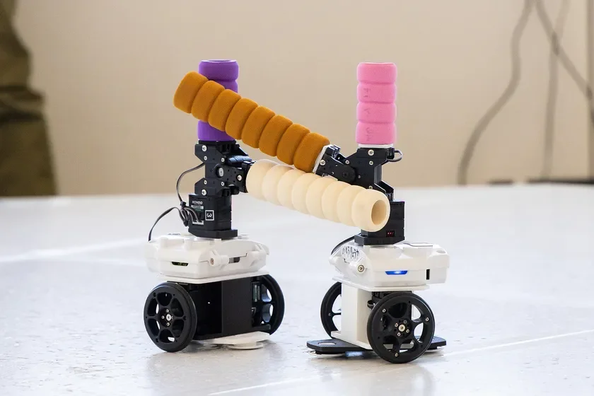 カラフルなフォームで覆われた棒で連結された2台の小型モバイルロボット